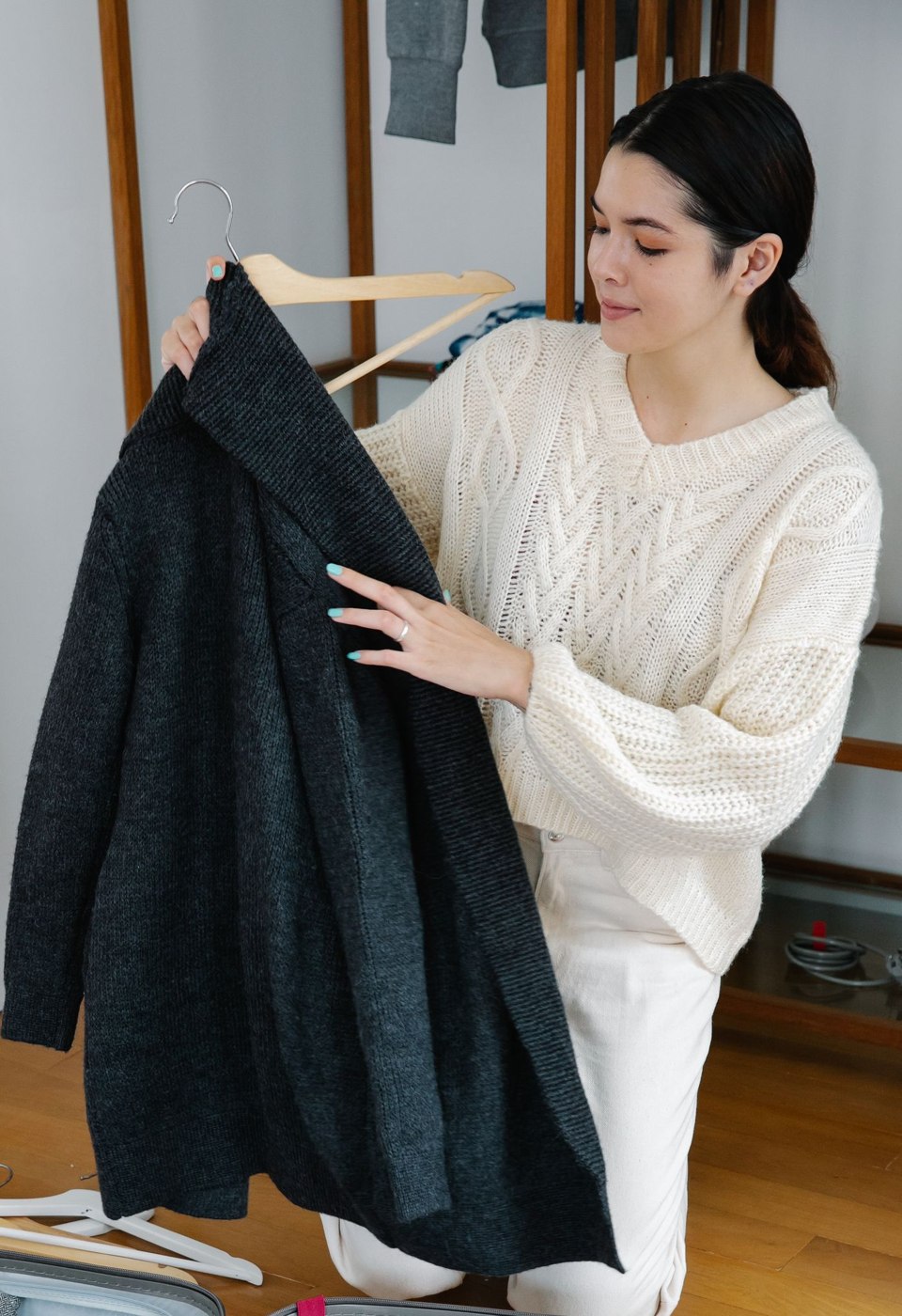 A Woman in White Knit Jacket Holding a Wooden Hanger with Black Coat
