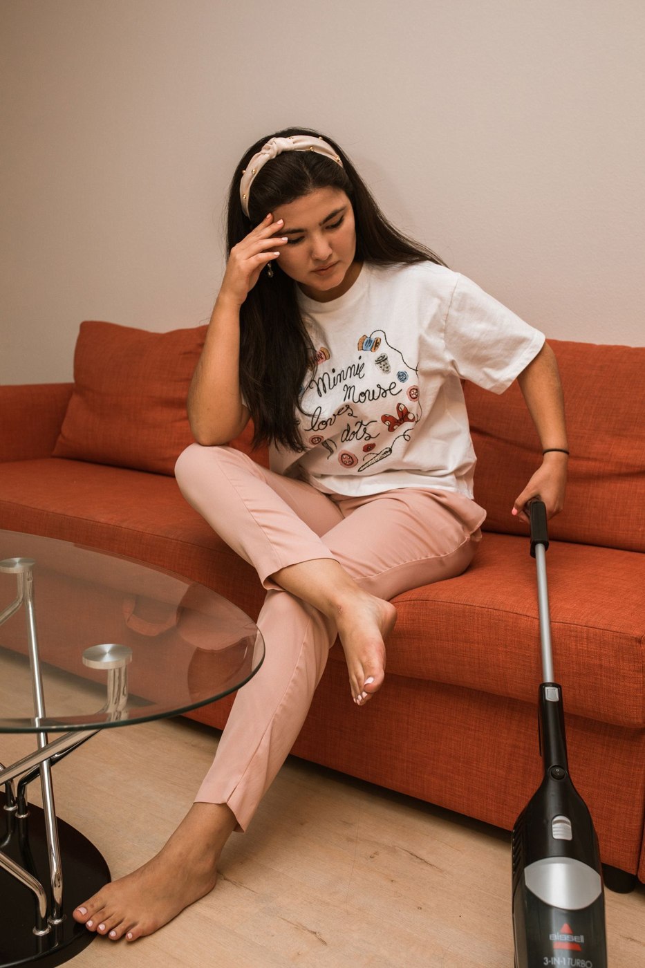 A Woman Sitting on a Couch while using a Vacuum Cleaner