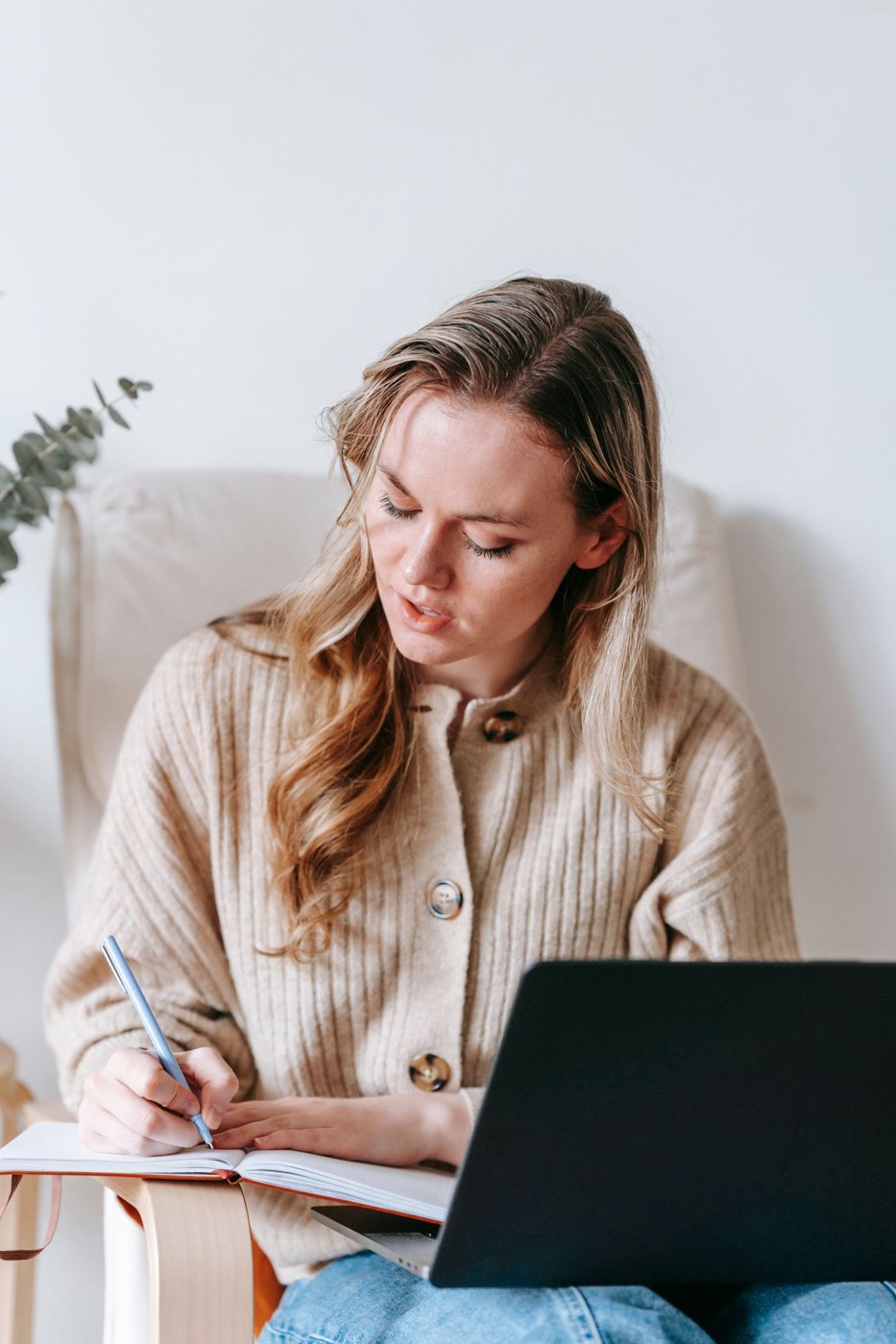 Focused woman with laptop writing in notebook in room